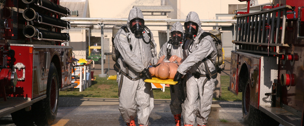 Some first responders in hazard suits carry a dummy on a stretcher